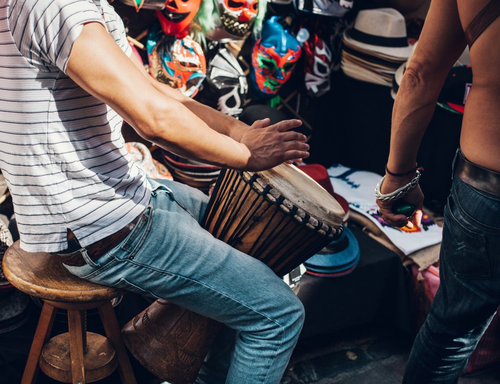 Hombre con camisa blanca a rayas tocando un djembé